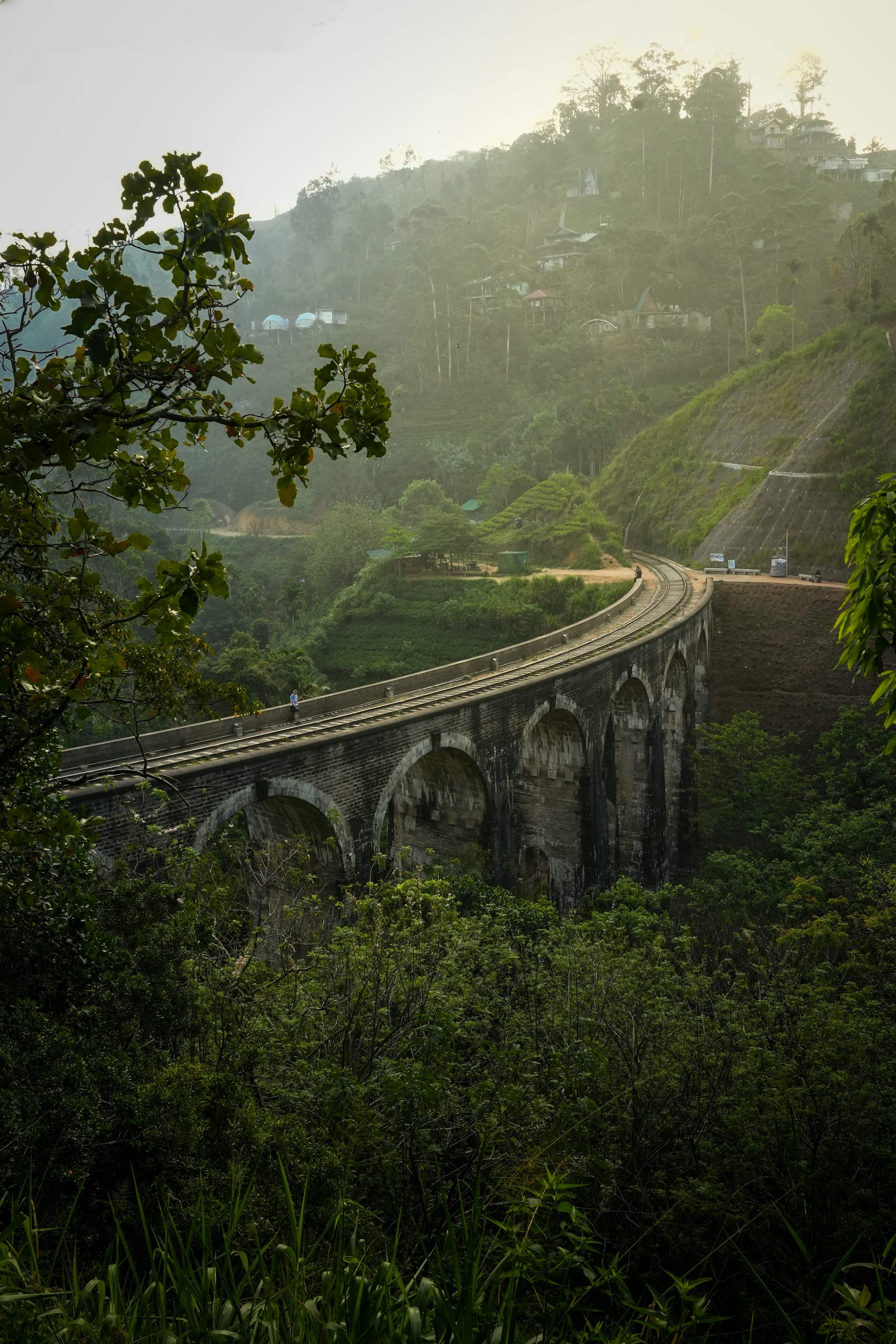 The stone arches of Nine Arch Bridge surrounded by dense green hillside forest