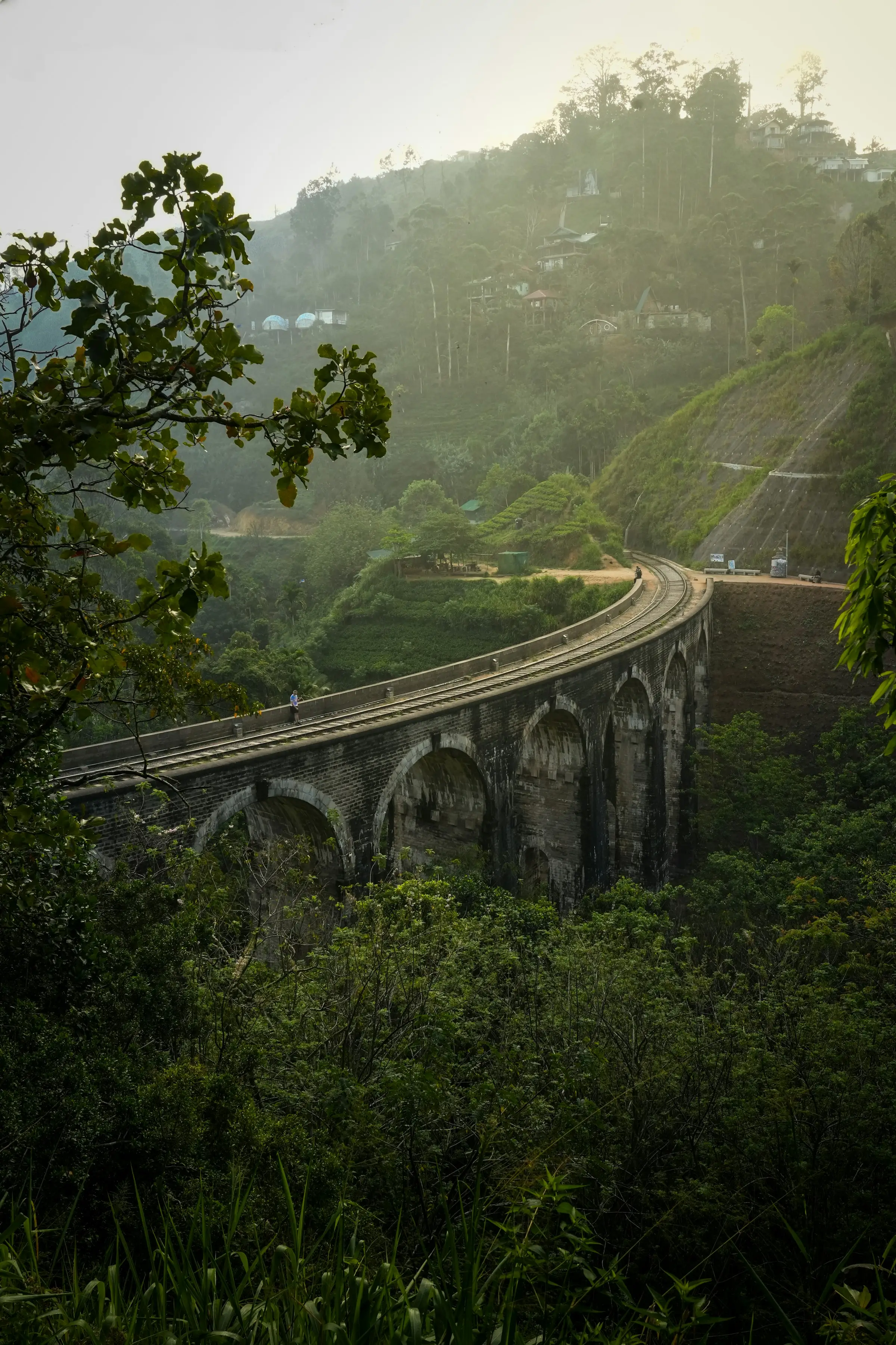 The stone arches of Nine Arch Bridge surrounded by dense green hillside forest