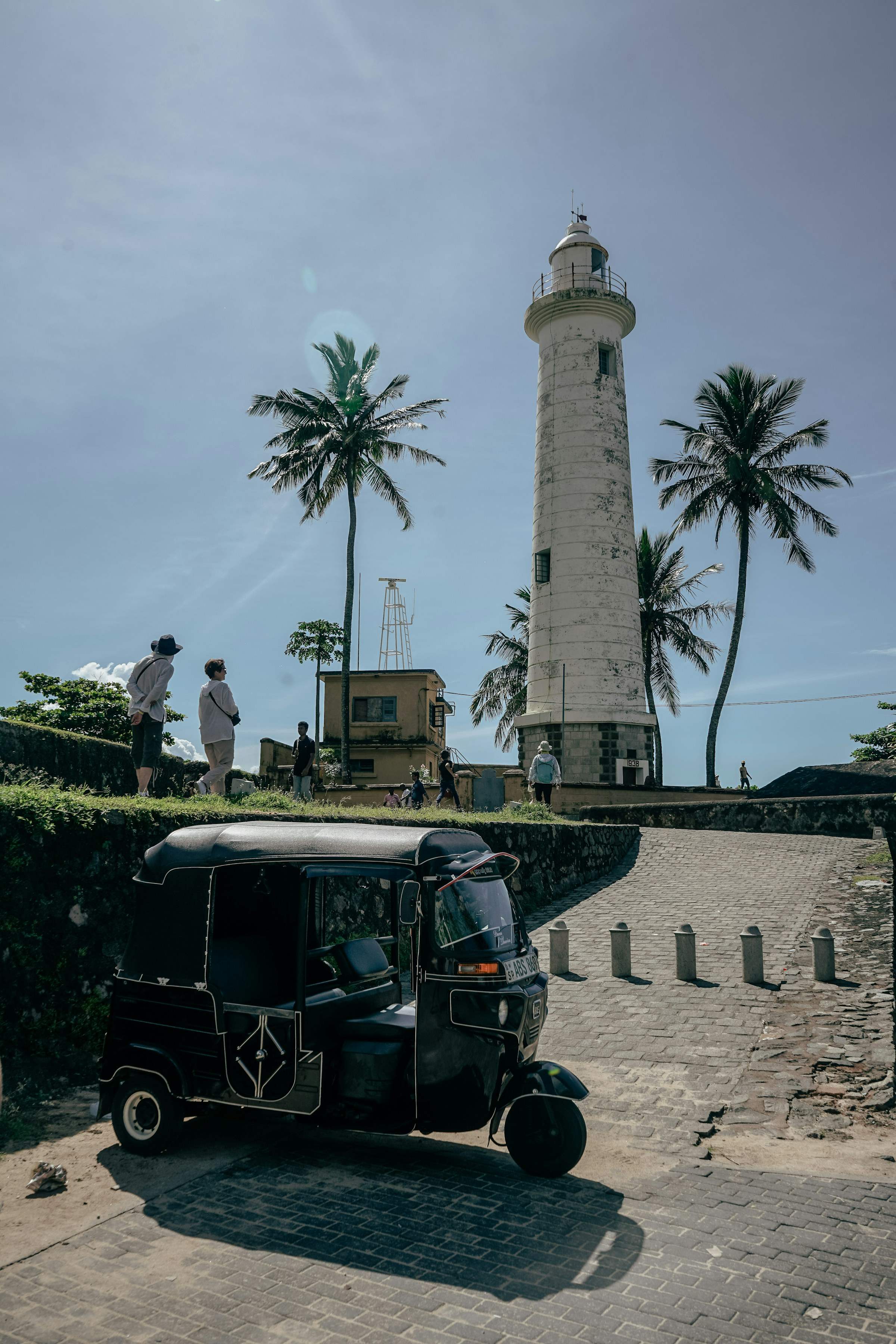 A tuk-tuk parked on a quiet street in front of the white Galle Fort lighthouse