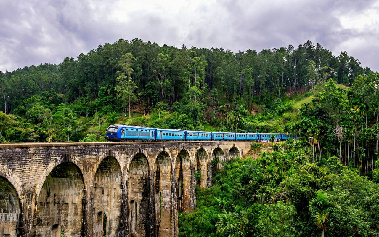 A blue train crossing the Nine Arch Bridge through dense green hills near Ella, Sri Lanka