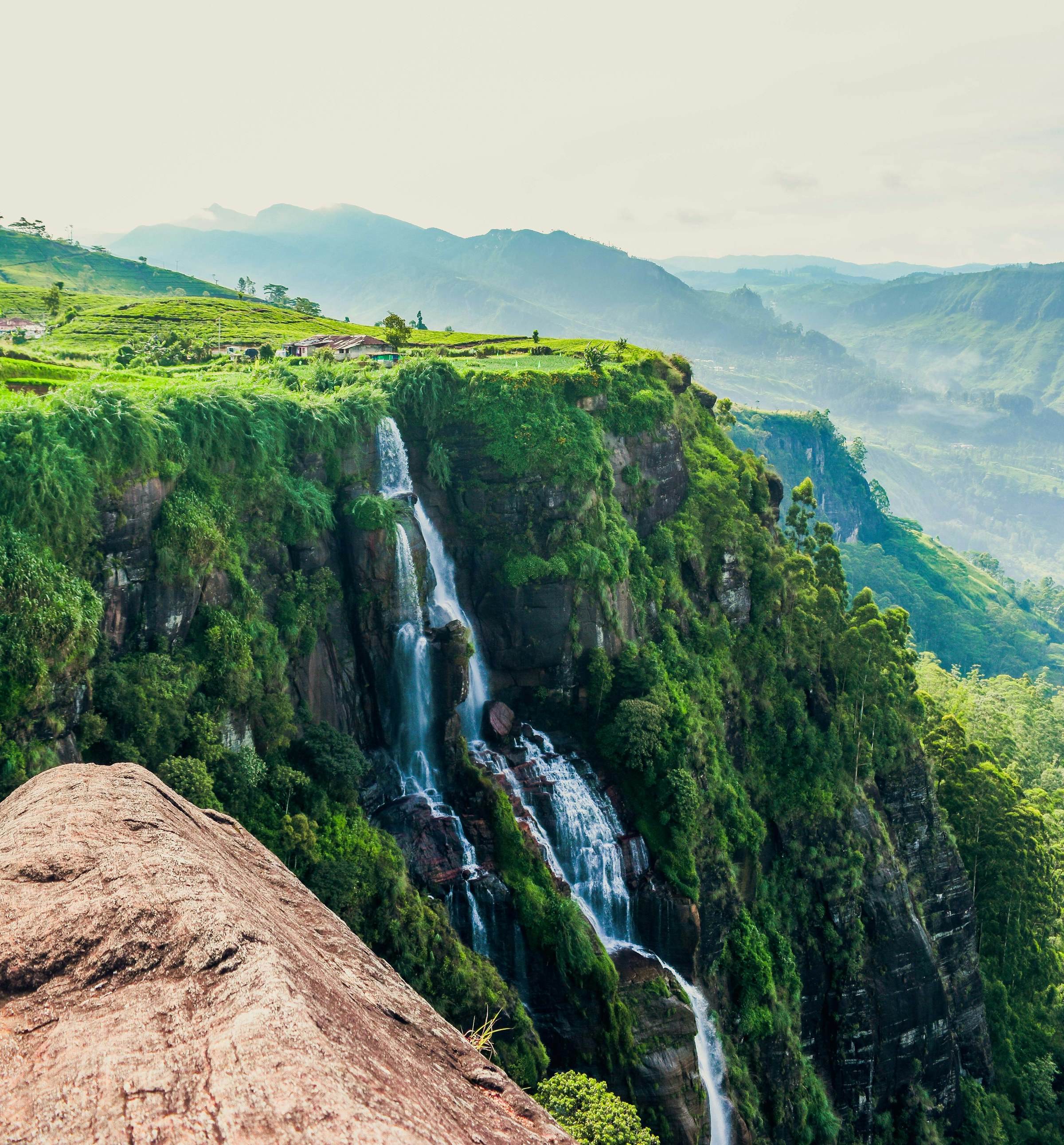 A waterfall dropping down a green cliffside into a misty valley