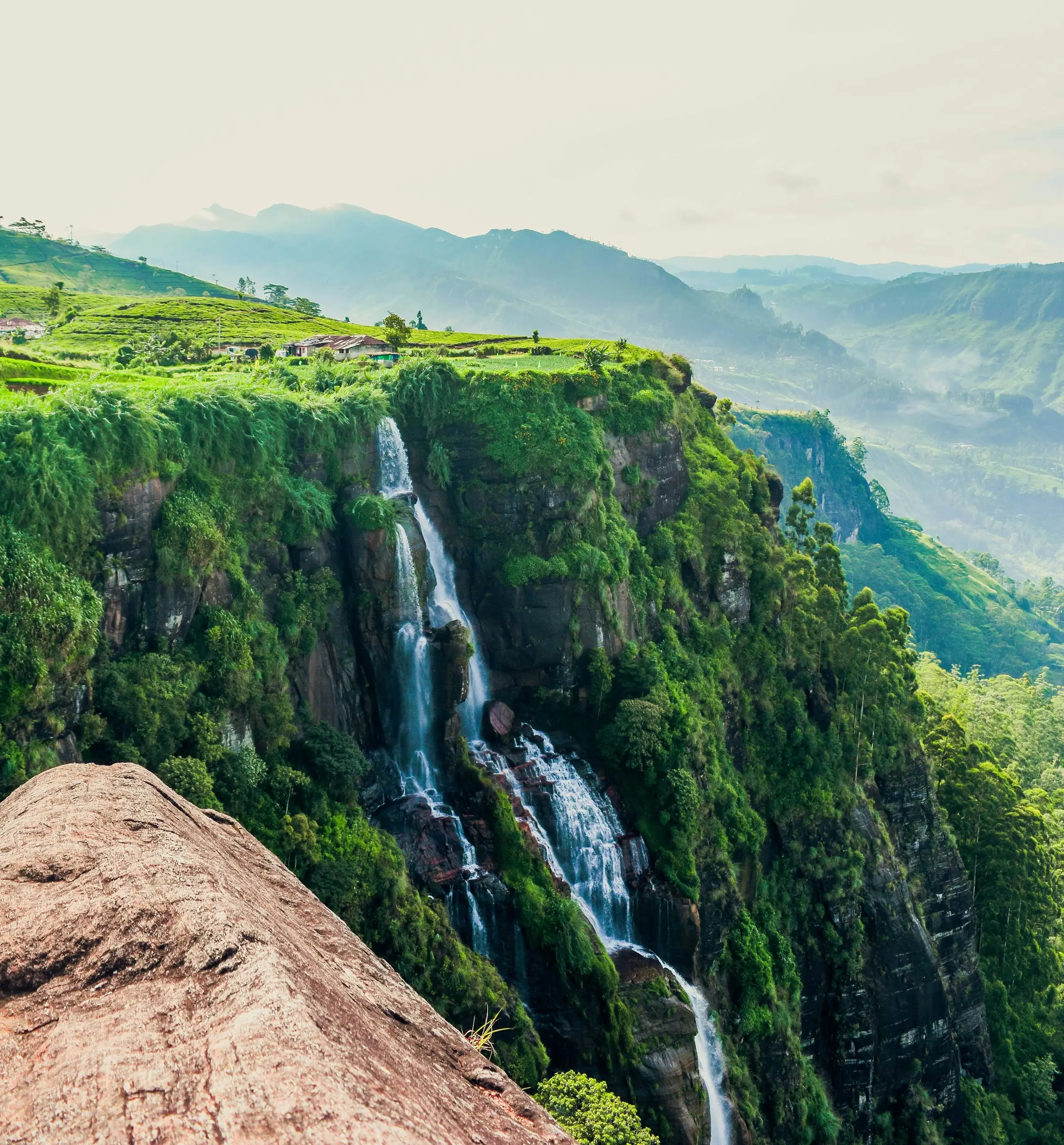 A waterfall dropping down a green cliffside into a misty valley